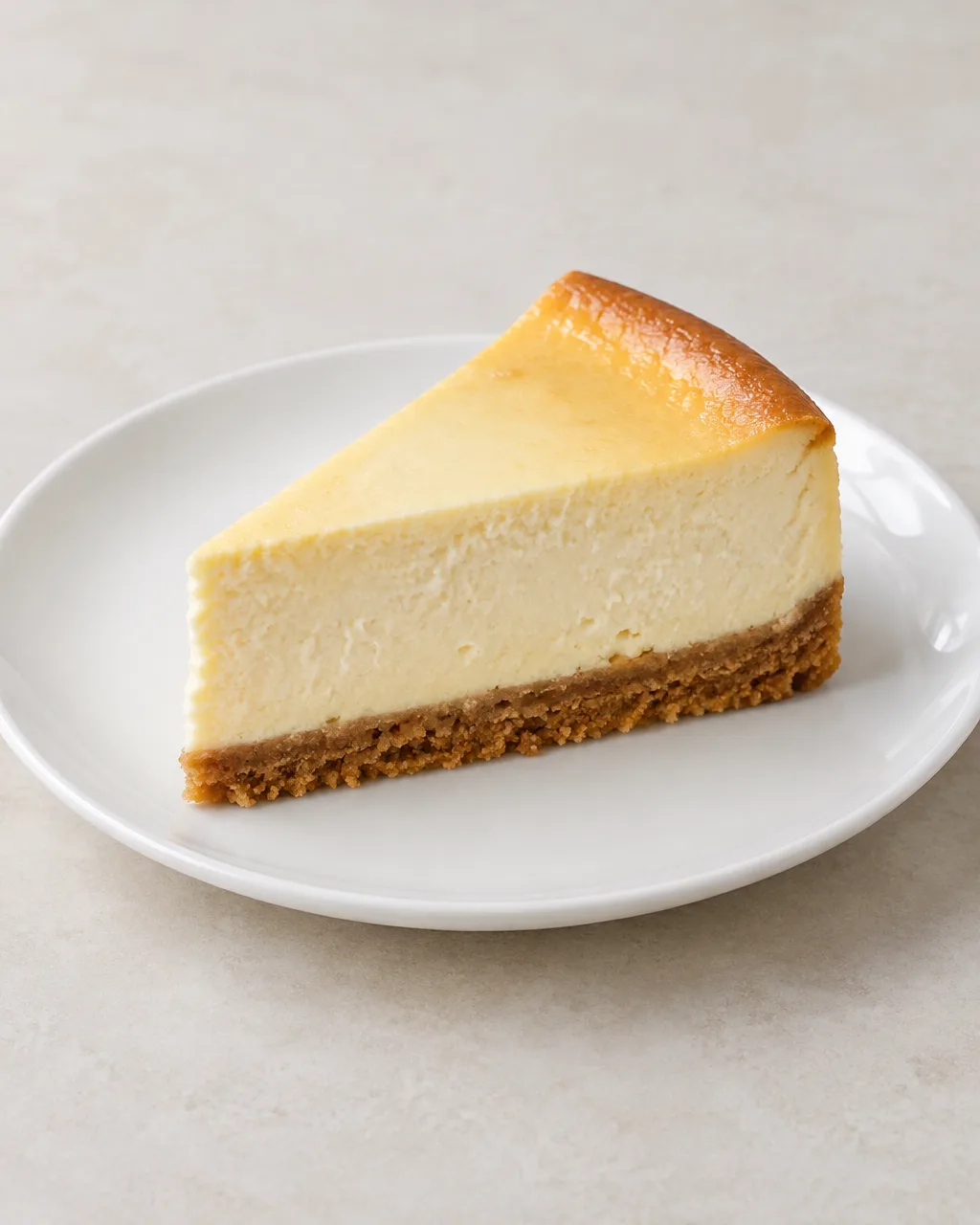Een punt New York cheesecake op een wit bord, met een goudbruine koekbodem en een dikke romige roomkaasvulling.